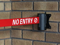 A barrier cartridge with a red tape and logo is mounted outside the building wall