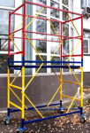 Mobilus statybinis bokštelis ant ratų šalia namo fasado.